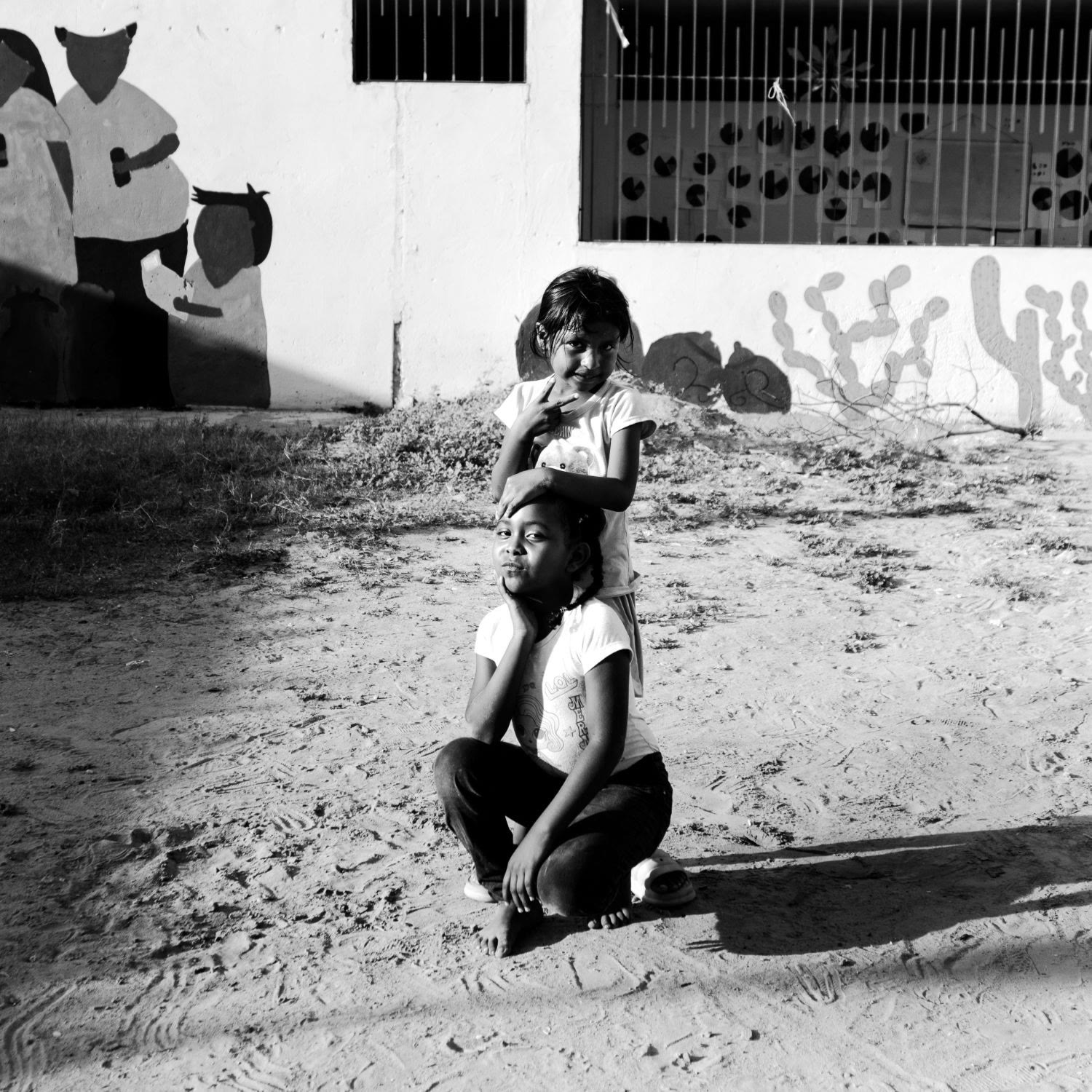 Dos niñas posando frente a un mural, en blanco y negro